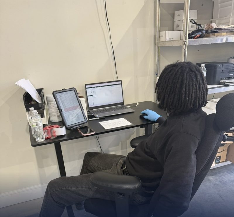 Team member processing orders at a desk with a laptop and tablet
